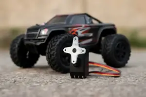Close-up of an RC vehicle’s servo motor with colorful wires, placed on concrete, with the vehicle blurred in the background.